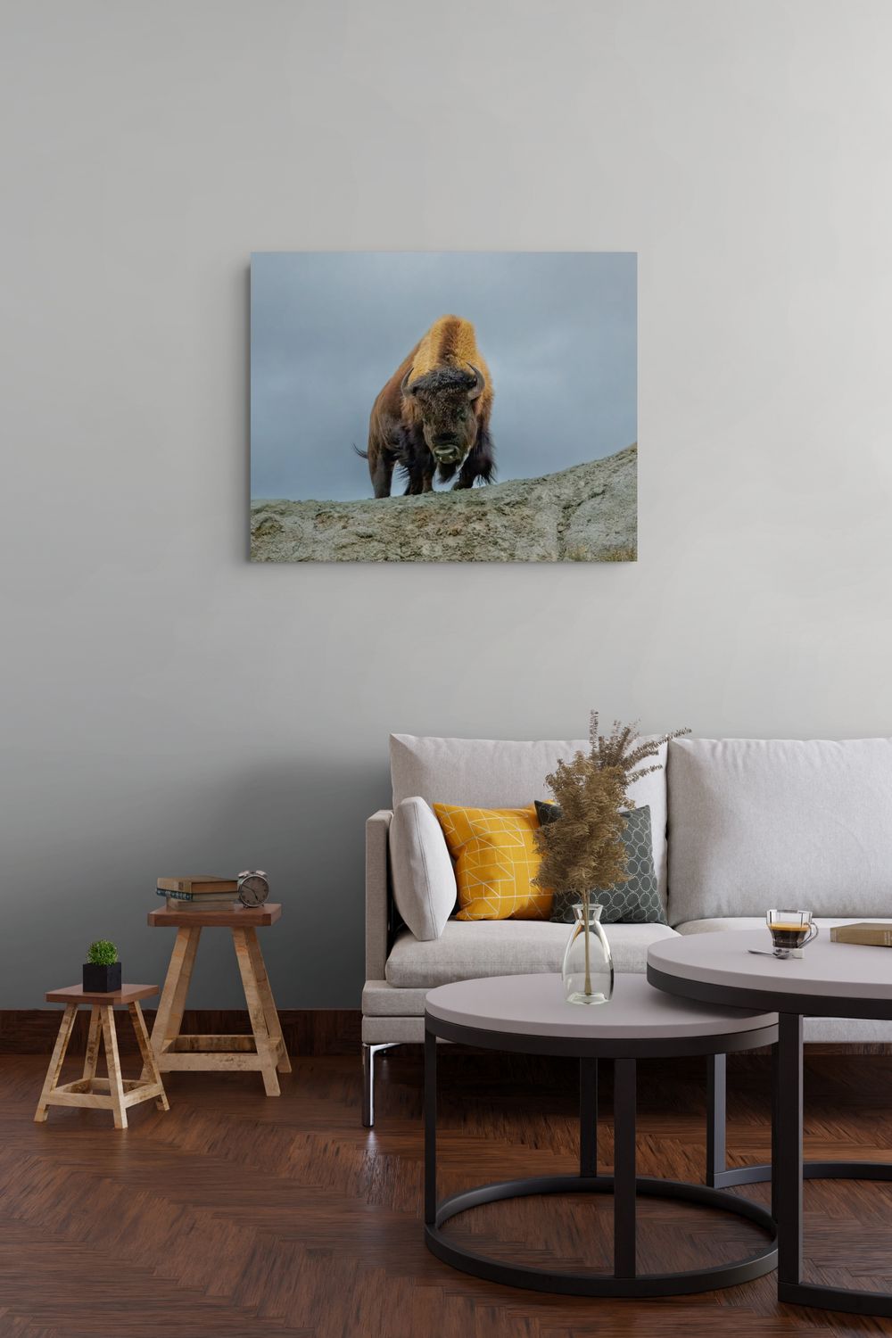 A square wall art print depicting a bison standing on a rocky outcrop under a cloudy sky, displayed above a modern white sofa in a living room setting.
