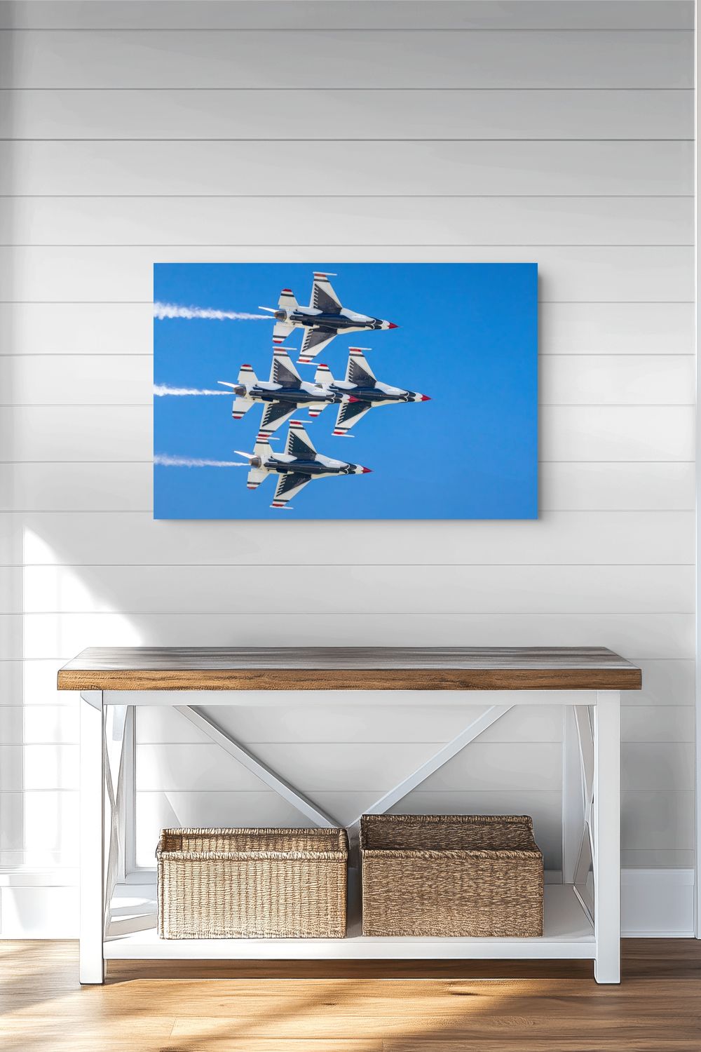 A rectangular wall art print showing four fighter jets flying in a blue sky, displayed above a wooden console table with woven baskets against a white shiplap wall.