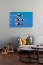A rectangular wall art print showing four fighter jets flying in a blue sky, displayed above a light gray sofa in a modern living room with wooden floors and round coffee tables.