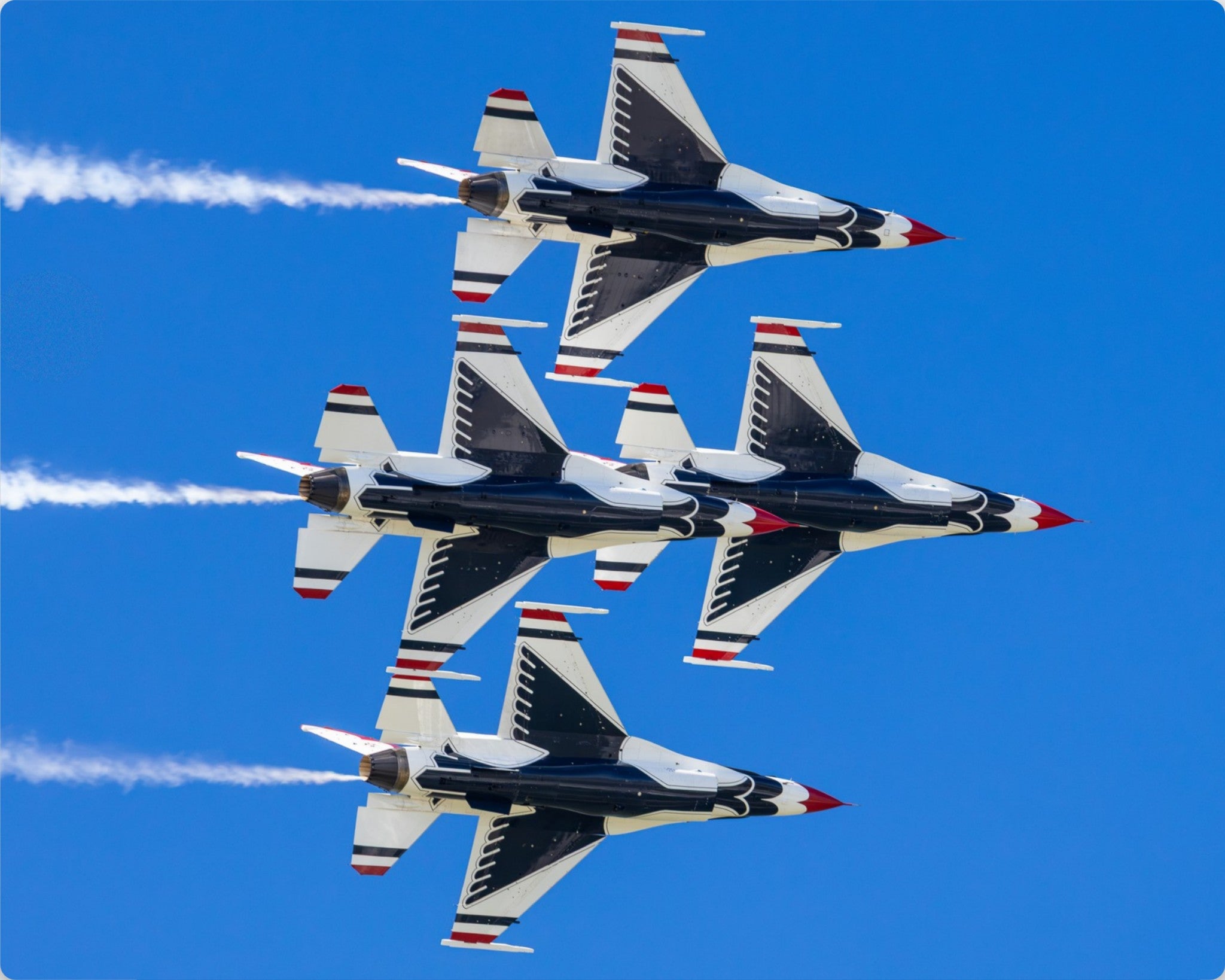 Formation of fighter jets performing aerial acrobatics against a clear blue sky.