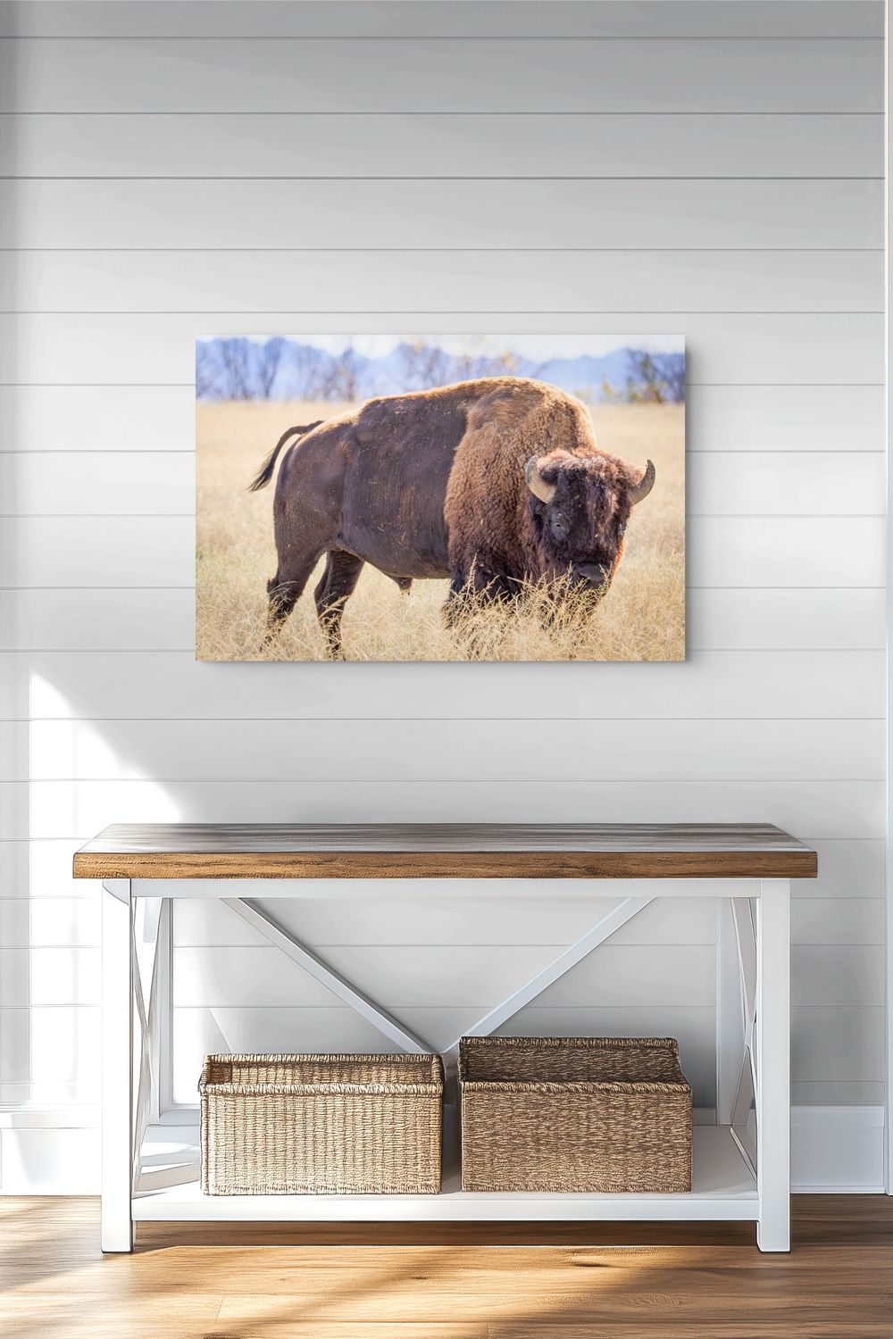 A rectangular wall art print showing a bison standing in a dry grass field, displayed above a white bench with a wood top in a bright interior setting.