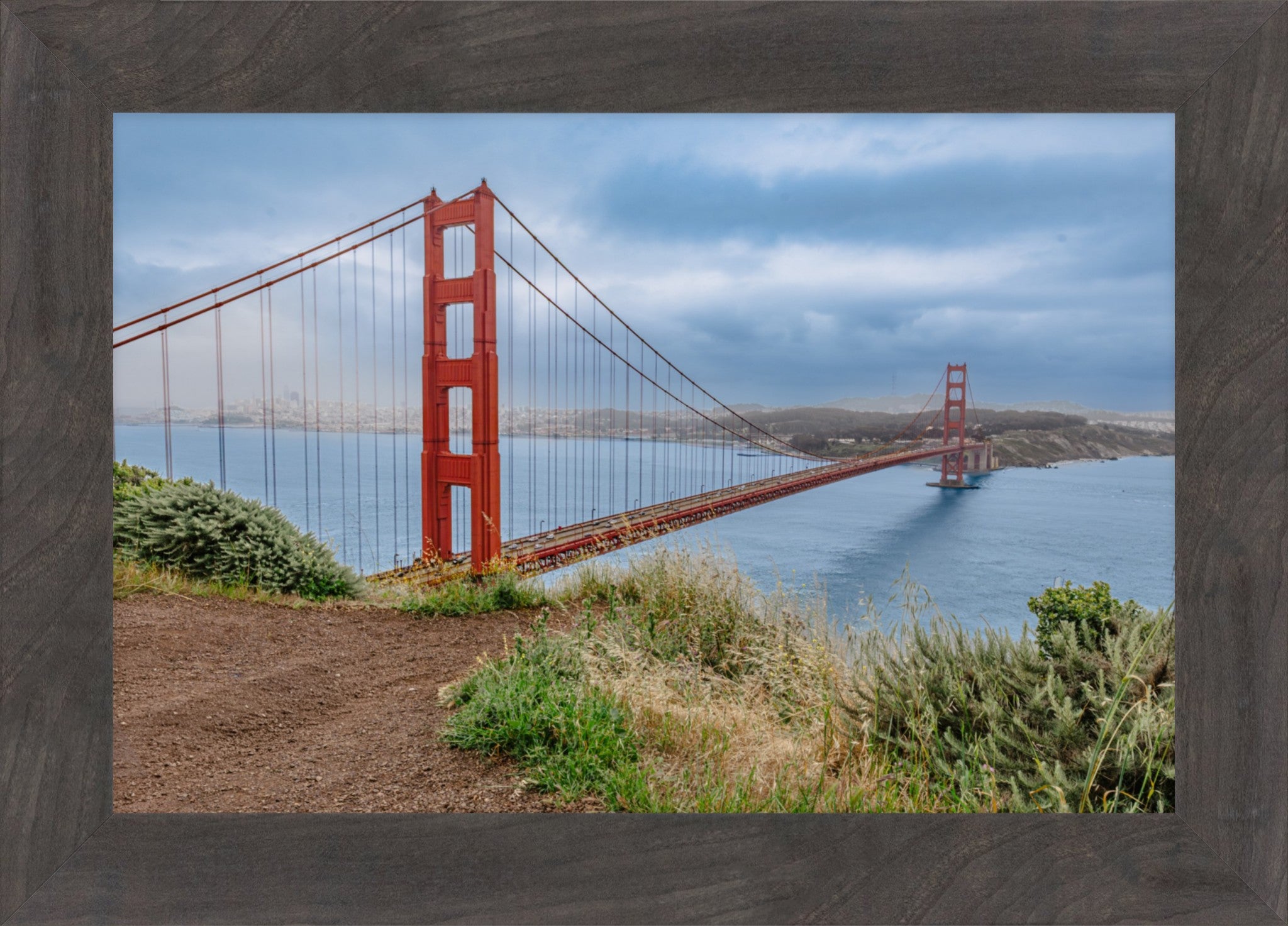 A framed photographic print of the Golden Gate Bridge over the water, with a dark wood frame visible around the image.