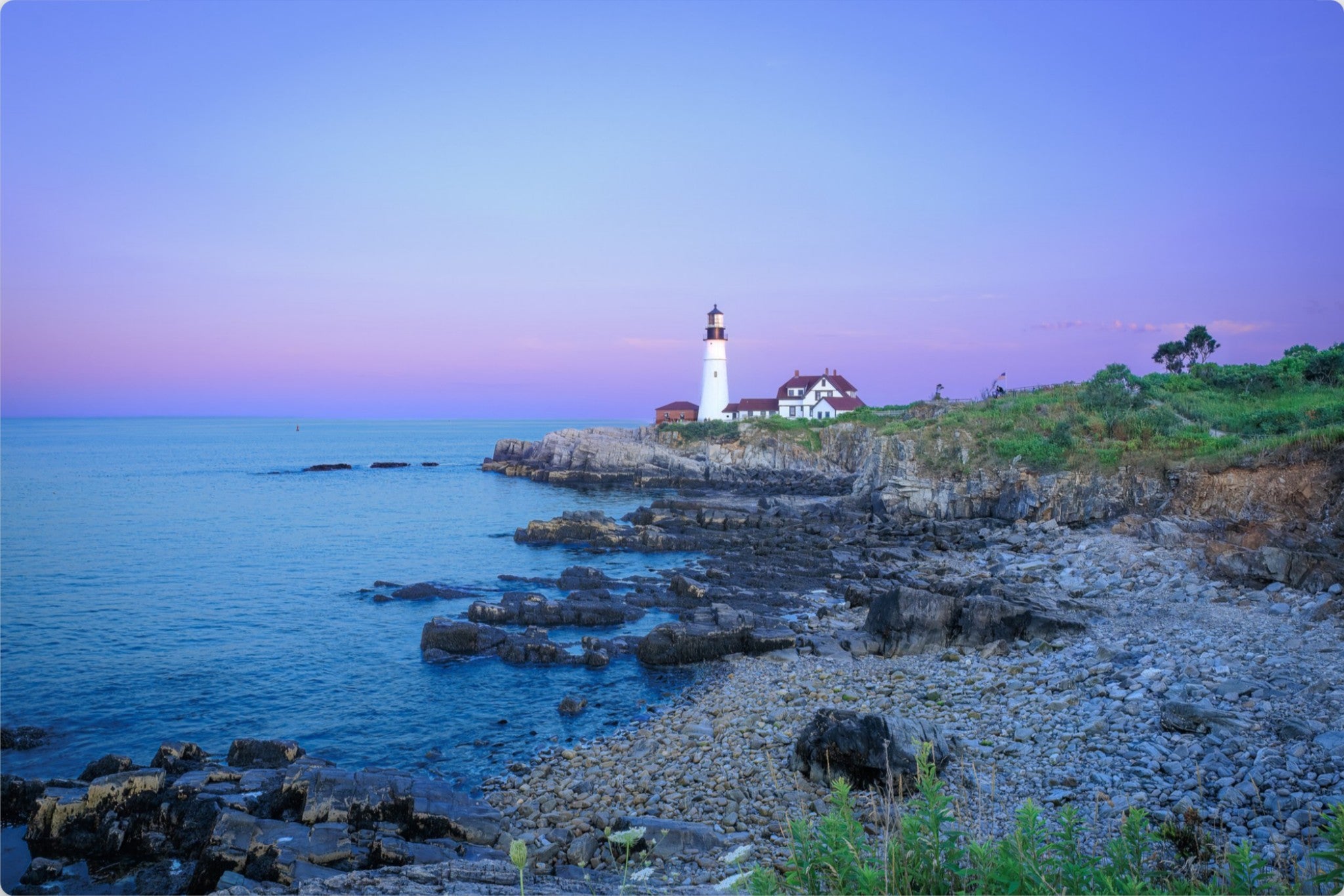 Coastal landscape print showing a white lighthouse on a rocky shoreline beside blue water under a purple and pink twilight sky.