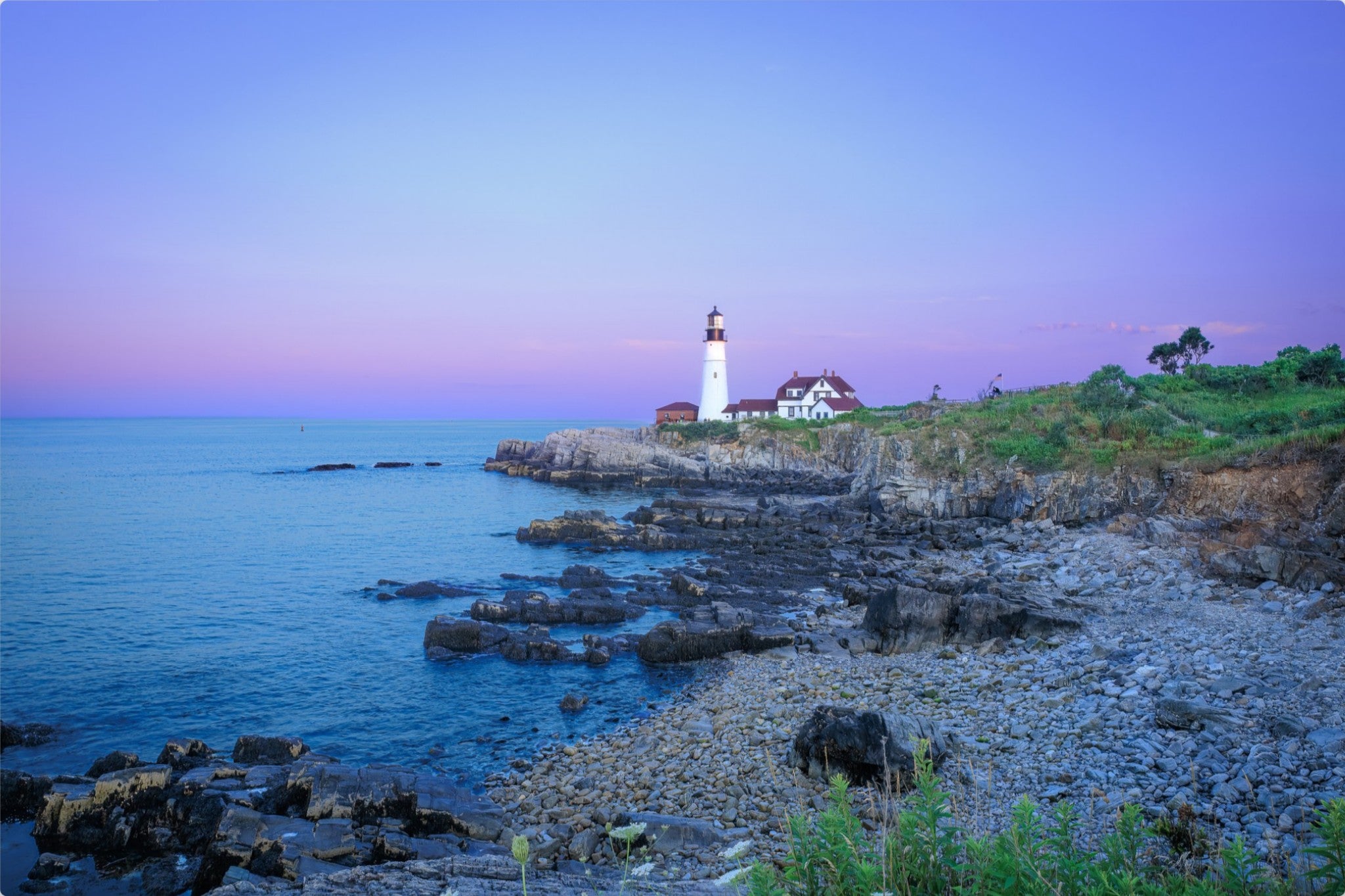 Lighthouse on a rocky coastline with a purple sky
